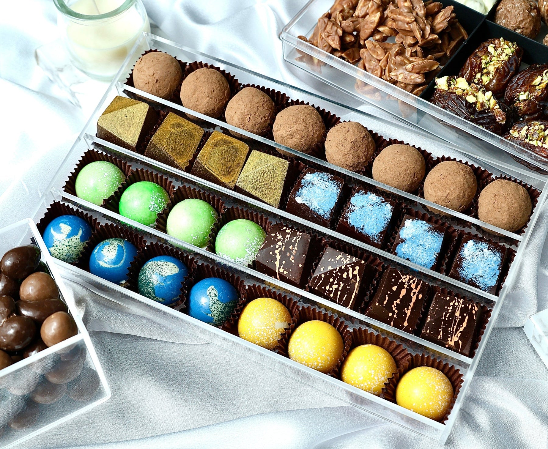 Assorted chocolates including truffles and marzipans in a box on a white surface.