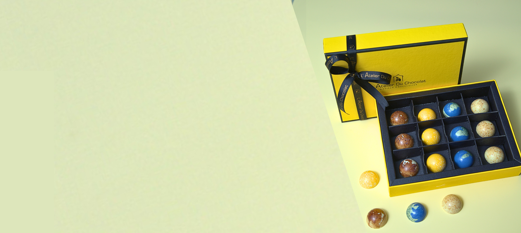 Yellow box with a bow containing assorted chocolates on a light green background