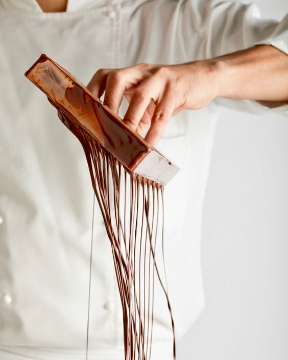 Person holding a spatula with chocolate frosting against a white background